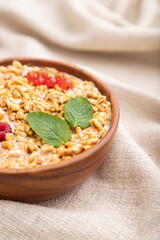 Wheat flakes porridge with milk, raspberry and currant in wooden bowl on white wooden background. Side view, selective focus.