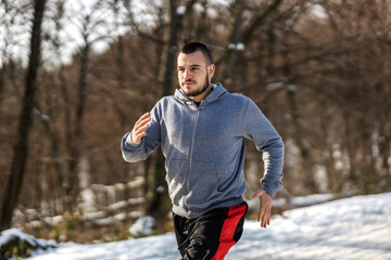 Sportsman running on snowy path in nature at sunny winter day. Winter fitness, cardio exercises, healthy habits