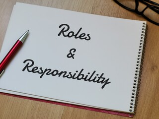 Text Roles and Responsibility on note book with pen and eye glasses on wooden table.