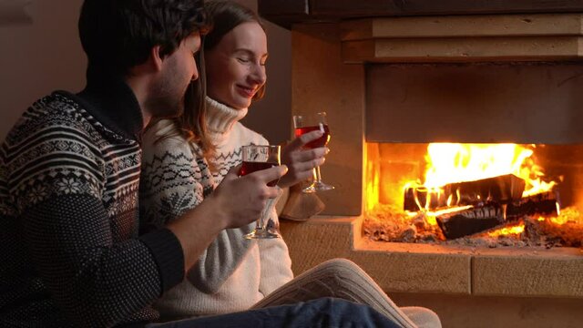 Young romantic couple sitting in front of fireplace at home, drinking red wine.