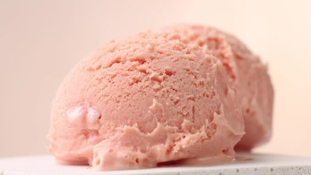 closeup of two pink ice cream scoops turning on beige background