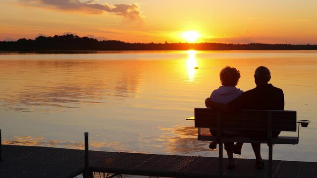 Silhouette of two people on a bench on a dock as they enjoy a sunset over a beautiful lake in Minnesota on a serene and relaxing evening, while a Canada goose swims by.