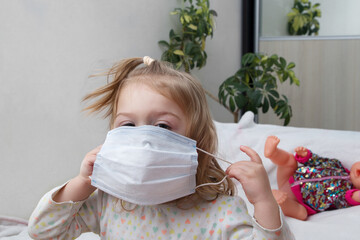 Little girl 2 years old playing with a medical mask at home - the new norm in real life