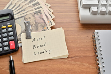 On the desk were Japanese yen bills, a keyboard, a notebook, and a word book with the word Asset...