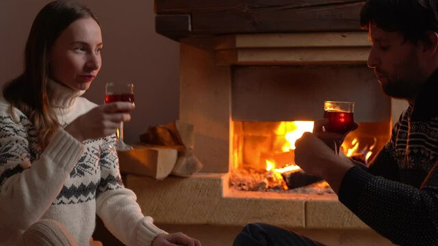 Young romantic couple sitting in front of fireplace at home, drinking red wine.