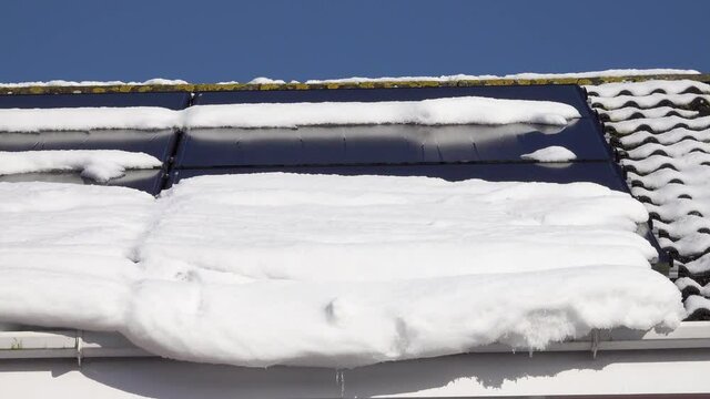 Melt water dripping from a rooftop in the early Spring. The snow reveals solar panels