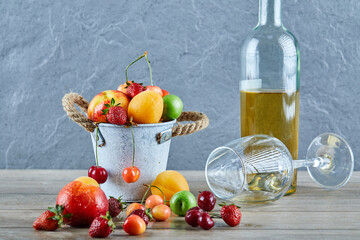 Bucket of fresh summer fruits, bottle of white wine and empty glass on wooden table