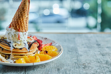 Pancakes with ice-cream cone, tangerine, strawberry, banana and chocolate syrup in the white plate...
