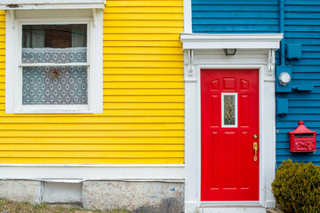 A bright red door of a building with blue and yellow wooden clapboard walls. The house has a red...