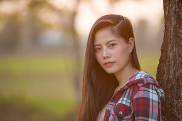 Naklejka premium A long haired beautiful woman standing by the tree in the green lawn at sunset