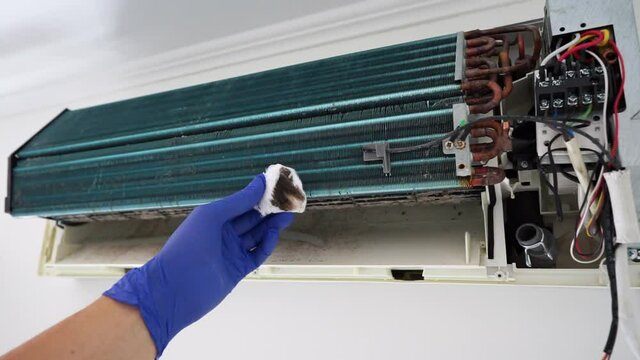 A service worker wearing a protective mask and gloves wipes the fungus inside the disassembled air conditioner with cotton wool and shows dirt on the cotton