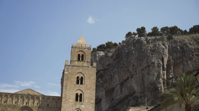 Bottom view of the ancient towers and a huge rock with growing trees on its top on blye sky background. Action. Concept of architecture.