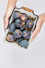 Hands holding a basket of purple figs on a white background