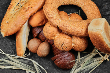 Slices of black bread, buns, bagel and baton on dark desk