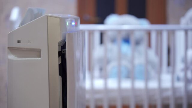 Modern air purifier humidifier in bedroom, working humidifier in front of baby cot creating a more comfortable environment at home. Climatic device