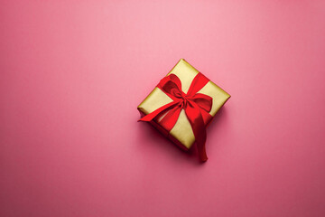 Holiday gift. Box in a gold gift wrapping with a red bow, on a pink background. Merry Christmas Valentine's Day greetings. Postcard with love. High quality photo