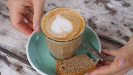 Hands taking away a glass of vegan cappuccino with heart art on it 