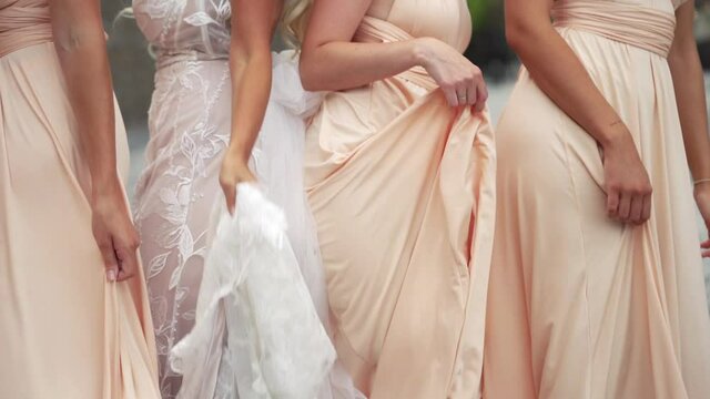 Bride and bridemaids dancing together outdoors in peach colored dresses and having fun - medium shot