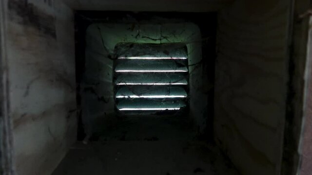 Camera moves into ventilation in a wall there cobwebs move in draft as air travels through louver.