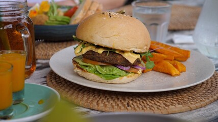 Person serving vegan meatless burger with sweet potatoes on a side on a woven placemat. 