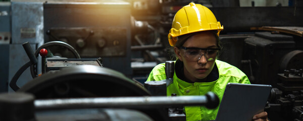 engineer woman wearing helmet and reflective vest in check and control industrial machine on tablet...