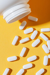 White pills are poured from a jar on a yellow background. Food supplement, multivitamins, medications