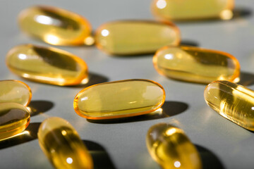Yellow gelatin capsules on a gray background. Food supplement, vitamin D, omega, vitamin C,...