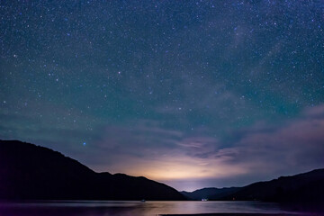 Fototapeta na wymiar starry sky above the shape of mountains with the light of a city in a fjord in the Marlborough Sounds, New Zealand