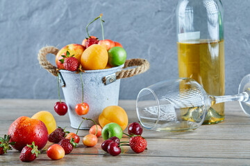 Bucket of fresh summer fruits, bottle of white wine and empty glass on wooden table