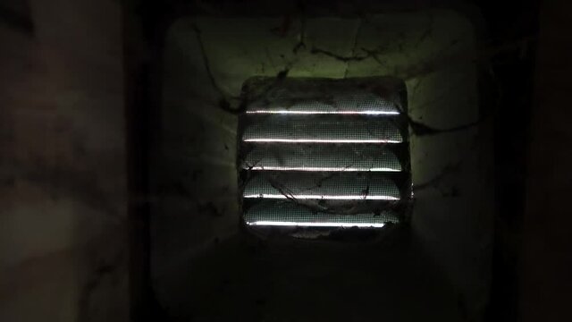 Cobwebs in ventilation duct. Camera moves from right to left. Spider web vibrate in air stream. Lights flow through ventilation louver.