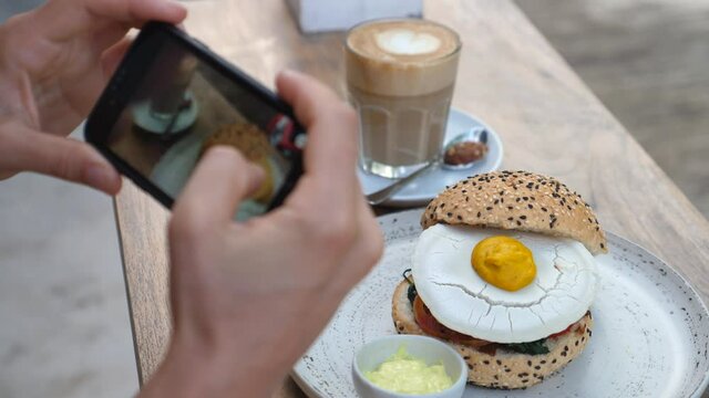 Food blogger taking pictures of vegan burger with plant based egg on top to share on social media 