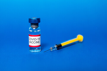 Vial with filled with Covid-19 vaccine and syringe on blue background