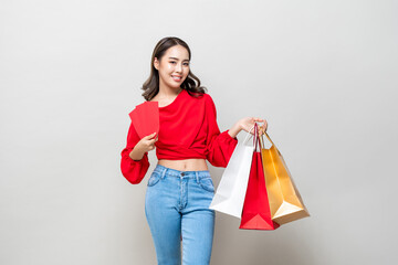 Fototapeta na wymiar Happy Asian woman holding shopping bags and red envelopes or Ang Pao isolated in light gray studio background for Chinese new year sale concept