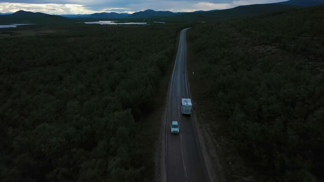 Aerial view overlooking a car passing a rv driving in polar nature, dark, summer day - tilt up, drone shot