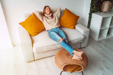 Obraz premium Calm satisfied woman relaxing or sleeping on the sofa in living room. Carefree lady resting at home, enjoying stress free weekend. Day off work. Home lifestyle, home comfort concept. 