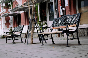 Two park benches with old building background. Bench was made of iron and wood. View from the front. 