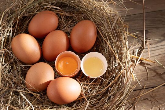 Several raw fresh chicken eggs in a nest of hay on a wooden background