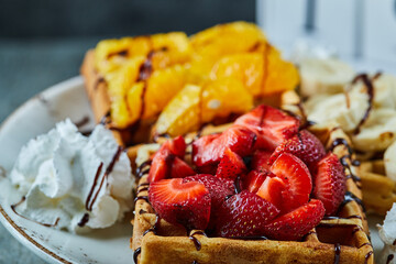 Waffles with ice-cream, banana, strawberry, chocolate in the white plate on the marble background