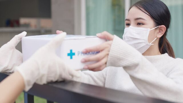Young attractive beautiful asian female receive medication package box free first aid from pharmacy hospital delivery service at home wear glove, face mask in telehealth, telemedicine online concept.