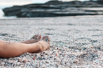 Side view of woman's feet lying on a beach full of seashells