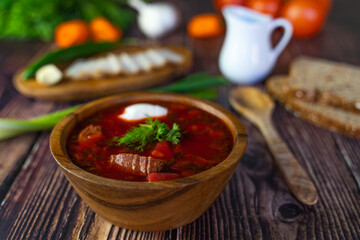 Borscht with sour cream in a wooden bowl on a wooden table. The table also contains black bread, bacon, green onions, peppers and garlic. Traditional Ukrainian and Russian cuisine.
