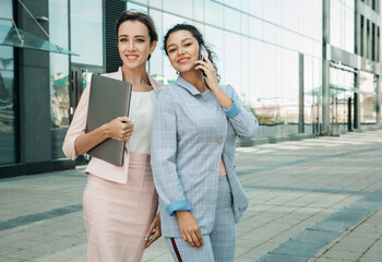 Business, people, tehnology and lifestyle concept: Two business women. One is holding a laptop, the other is talking on the phone. Mixed races. Caucasian woman and African woman.