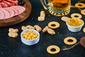 A plate of sausages, various snacks and a glass of beer on dark table