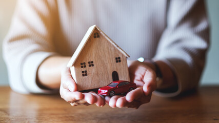 Closeup image of a woman holding and showing car figure model and wooden house model