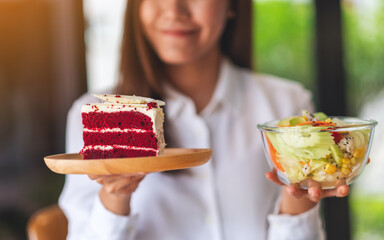 Closeup image of a young woman holding a plate of velvet cake and a bowl of vegetables salad