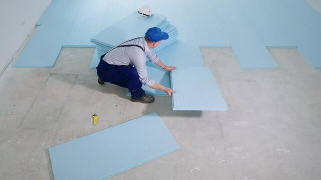 floor insulation, young professional male construction worker lays down styrofoam to prepare room for laminate flooring at construction site