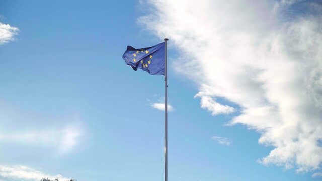 EU flag waving on its own in strong wind on a blue and cloudy sky, symbol of the European Union alliance