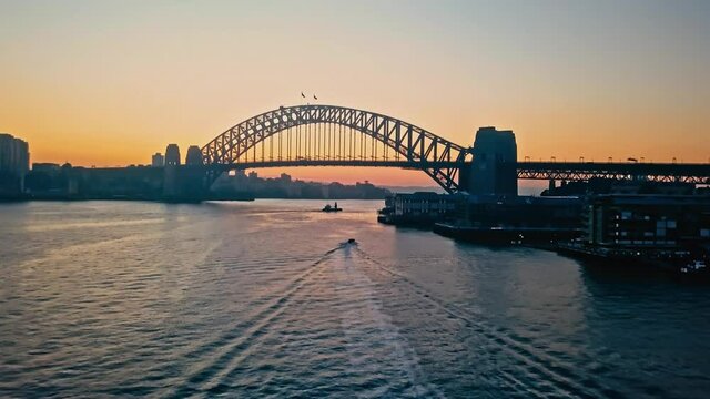 Drone flight over the water with a tilt-up to reveal the Harbour Bridge at sunrise. 