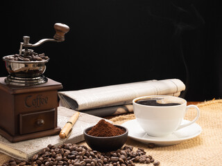 Steam white coffee cup with grinder, roasted beans,coffee ground and note book over burlap hessian  on grunge wood table background