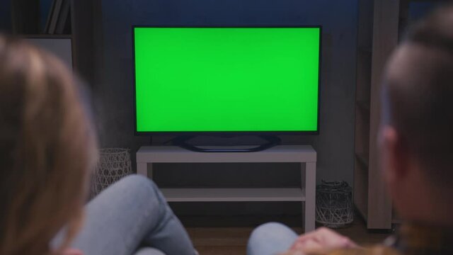 Family Couple Watches Green Screen TV Mockup Sitting on Couch in Living Room Together. Rear View on Casual People who Watching TV Green Screen in Domestic Cinema. Looking TV Show or News in Home Rest
